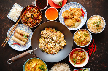 Asian food set. Noodles, fried rice with chicken, tom yum soup, spring rolls, deep fried fish and udon with prawns. Top view on dark rustic background. Oriental style food concept composition.