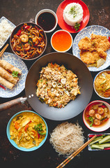 Asian food set. Noodles, fried rice with chicken, tom yum soup, spring rolls, deep fried fish and udon with prawns. Top view on dark rustic background. Oriental style food concept composition.