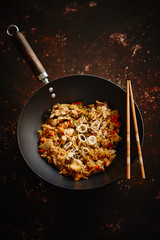 Delicious fried rice with chicken. Prepared and served in a wok with soy and sweet sour souces on side. Placed on dark rusty background. Top view.