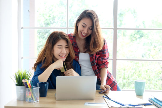  Two young asian women holding credit card and using laptop computer for shopping on line with happiness, business and technology concept, digital marketing, casual lifestyle