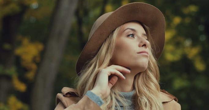 Close up of the pretty young blonde woman in a hat and romantic mood thinking about something and dreaming while being in the park at fall. Portrait.