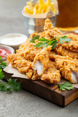 Breaded chicken strips with two kinds of sauces and fried potatoes on a wooden Board. Fast food on dark brown background
