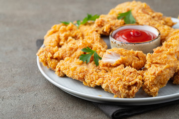 Breaded chicken strips with tomato ketchup on a white plate. Fast food on dark brown background