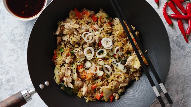 Delicious fried rice with chicken. Prepared and served in a wok with soy and sweet sour souces on side. Placed on stone background. Top view.