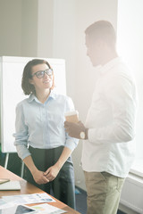 Obraz premium Positive confident multi-ethnic marketing specialists standing at table and discussing sales of new product while drinking coffee in modern office