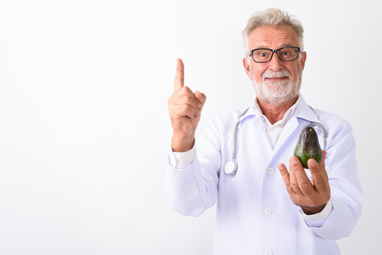 Studio shot of handsome senior bearded man doctor holding avocad
