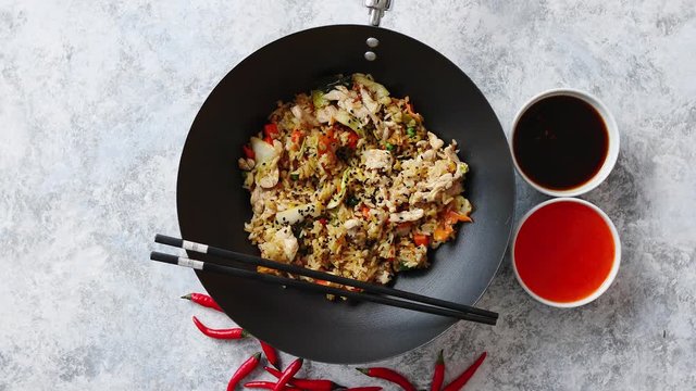 Delicious fried rice with chicken. Prepared and served in a wok with soy and sweet sour souces on side. Placed on stone background. Top view.