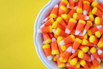 White bowl full of Halloween candy corn on a yellow background
