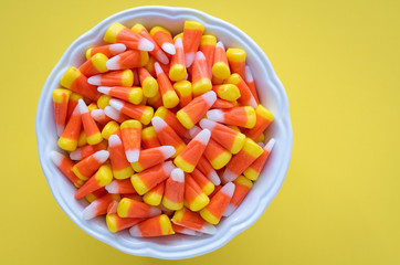 White bowl full of Halloween candy corn on a yellow background
