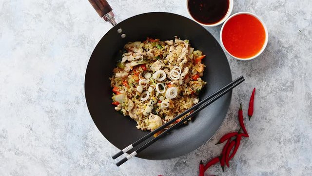 Delicious fried rice with chicken. Prepared and served in a wok with soy and sweet sour souces on side. Placed on stone background. Top view.