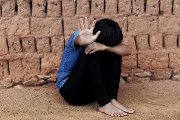 Helpless little girl sitting on floor against old earth brick wall,stop violence and abused children,human trafficking concept