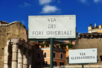 Imperial Fora Avenue and Alessandrina Street old marble road sign with ancient ruins background in...
