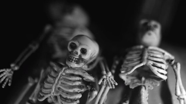 Small plastic skeletons draped over a Halloween pumpkin.  Closeup, low light.