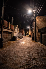 Dark and eerie urban city cobblestone brick paved alley at night