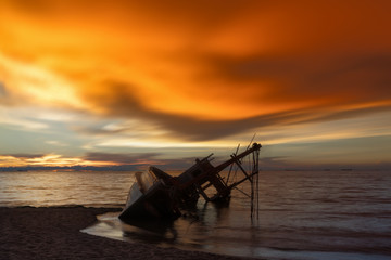 Abandoned shipwreck of wood fishing boat on beach at twilight time