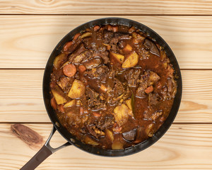 Close-up of colorful goat stew in cooking pan on top of  wooden table.