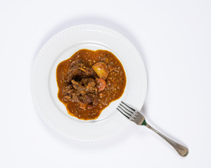Close-up plate of colorful goat stew with potatoes, carrots, onions, bay leaf, and other spices.