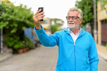 Happy handsome senior bearded man smiling while taking selfie pi