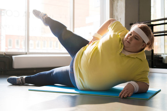 Full Length Portrait Of Obese Young Woman Stretching Legs While Working Out In Fitness Club