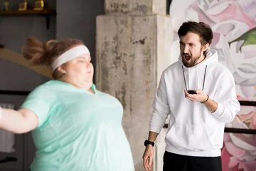  Portrait of angry coach shouting at  obese young woman in fitness club, copy space © Seventyfour