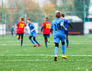 Obraz premium Children are kicking soccer classic white and black ball. Young kids football action. Boys are running after the Ball on green artificial grass. Footballers in blue and red shirts