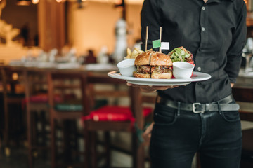 Big tasty burger with fresh salad served by waiter with black costume