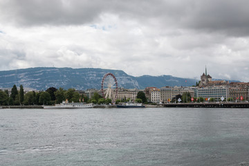 Fototapeta na wymiar Geneva, Switzerland - June 29, 2017: View on lake and city Geneva, away mountains. Summer landscape, sunshine weather, dramatic cloudy sky