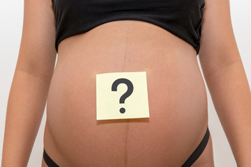 Belly of a young pregnant woman with a white sticker and a question on it