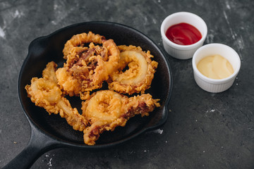 fried squid rings breaded on the black pan with grey concrete background