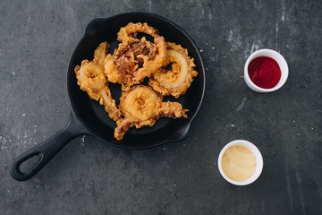 fried squid rings breaded on the black pan with grey concrete background
