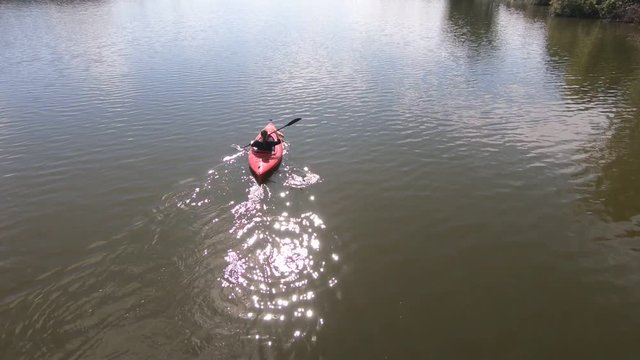 Woman Paddles A Red Kayak In A Lake. Drone Flies Overhead And Pans Up.