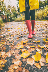 Red rubber boots woman walking in autumn leaves street in park. Fall fashion lifestyle.