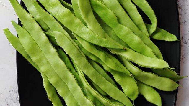 Black ceramic plate with fresh green bean pods placed on white rusty table. Top view shot with copy space.