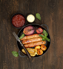 grilled, juicy sausages in a pan on a wooden background