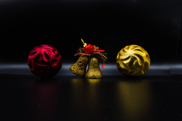 Red and yellow christmas balls and glittered bell on black.