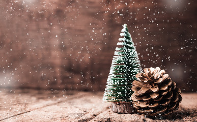 Christmas tree and gold pine cone and snow falling on grunge wood table and dark brown wooden wall.Winter Merry Christmas holiday greeting card.