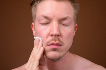 Fototapeta premium Young handsome man shirtless while grooming against brown backgr