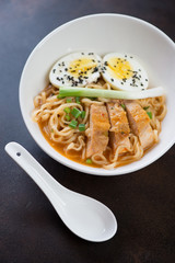 White bowl with chicken ramen noodles on a dark brown metal background, vertical shot
