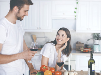 Beautiful young couple is drinking wine and smiling while cooking in kitchen at home.