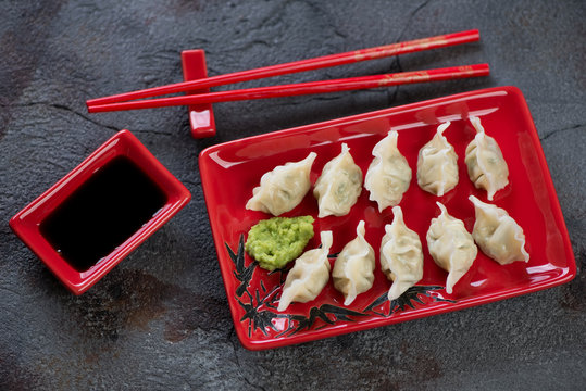 Red tableware with boiled wontons and a dipping sauce, high angle view over grey asphalt background