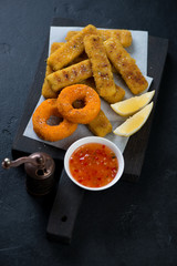 Fried calamari rings and fish sticks or breaded fish fillet with lemon and dipping sauce, black...