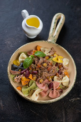 Farfalle pasta with tuna fillet, red beans and corn in a serving pan over dark brown stone background, vertical shot