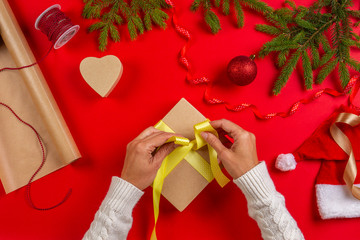 Christmas gift wrapping. Woman's hands packing Christmas present box on red table background