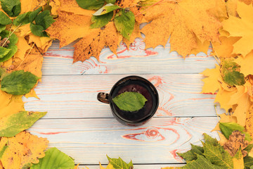 tea in a dark transparent cup with autumn leaves on a blue wooden table, in a cup a leaf of autumn.