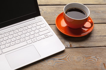 A cup of coffee on the orange plate on the wooden table. Office interior
