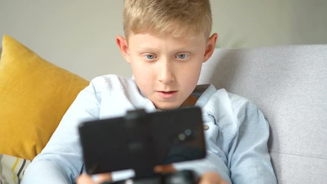 Teenager boy lying on the cozy sofa and  enthusiastically plays game using the gamepad with smartphone. Health vision concept 4K UHDTV footage