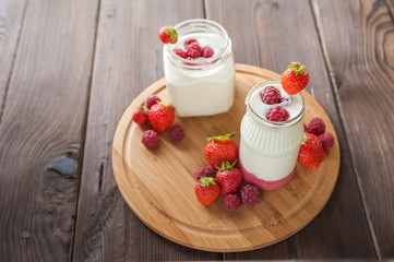 Two cans of milk yogurt with fresh raspberries and strawberries on a round wooden board close-up