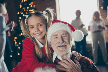 Close-up portrait of joyful girl hugging grandpa in headwear. No