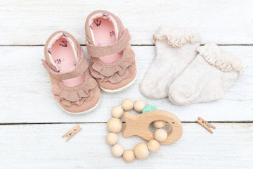 Baby pink sandals, socks and teether on a wooden background