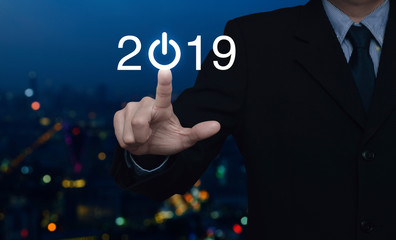 Businessman pressing 2019 start up business icon over blur colorful night light city tower and skyscraper, Happy new year 2019 concept